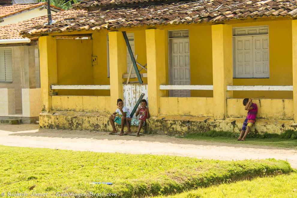 Imagem de três crianças sentadas na frente de uma casa amarela na Vila da Cova da Onça.